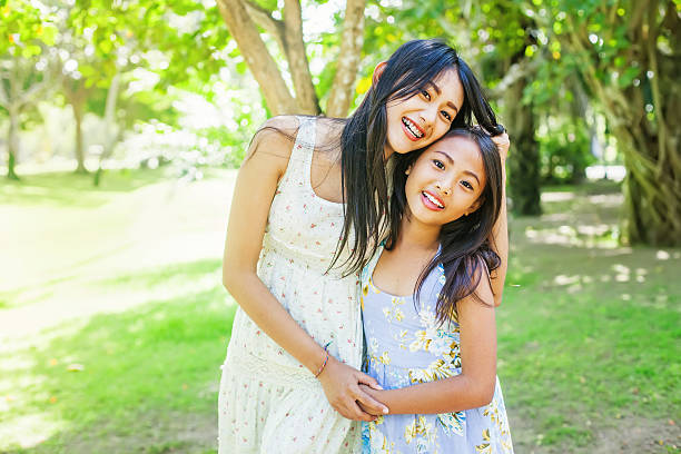 A couple of asian sisters hugging each other on a background of a summer park